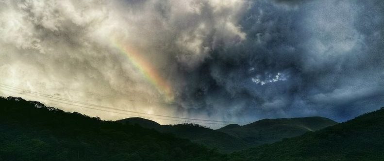 paisagem com montanhas e nuvens carregadas com parte de um arco-íris 